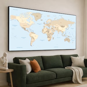 May include: A large framed world map with a black border hangs above a green sofa. The map features a light blue ocean and tan landmasses, with country names labeled. Decorative pillows in white and orange rest on the sofa.