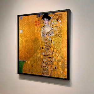 Könnte beinhalten: Ein Gemälde einer Frau in einem goldenen Kleid mit goldenem Hintergrund. Die Frau trägt eine Krone und eine goldene Halskette. Das Gemälde ist in einem schwarzen Rahmen.