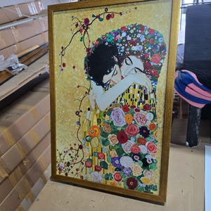 Pu&ograve; includere: Un dipinto incorniciato che rappresenta una coppia che si abbraccia, circondata da fiori colorati. Il dipinto &egrave; su sfondo dorato e presenta un motivo a mosaico sugli abiti dell'uomo.