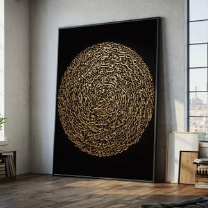 May include: Large framed artwork featuring a circular design of gold calligraphy on a black background. The artwork is leaning against a wall in a room with a window and wooden floor. The calligraphy is intricate and detailed.