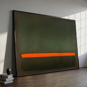 May include: Large framed abstract painting with a dark green background and a horizontal orange stripe. The artwork is leaning against a white wall and a wooden floor. A small vase and a stack of books are in the foreground.