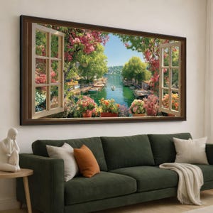 Puede incluir: Una obra de arte enmarcada que representa una ventana abierta con vistas a un canal pintoresco. El marco de la ventana es marrón y la vista incluye barcos, vegetación exuberante y flores coloridas. La obra cuelga sobre un sofá verde.