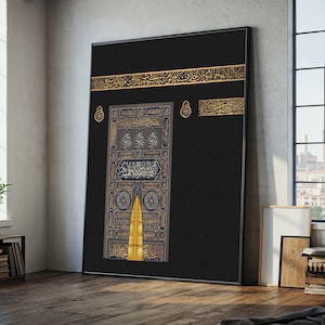 May include: Large framed artwork depicting the Kaaba in Mecca. The image features a black cloth with gold calligraphy and a golden door. The artwork is displayed in a room with a wooden floor and a window.