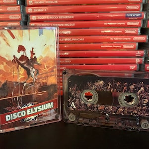 May include: A clear cassette tape with the title "DISCO ELYSIUM" in red and white. The cover art features a figure on horseback against a sunset backdrop. A second cassette is visible, with detailed artwork. The background shows a stack of Nintendo Switch game cases.