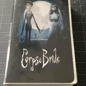 May include: A VHS tape of the animated film "Corpse Bride." The cover features a dark background with the title in white, stylized lettering. The artwork depicts a skeletal man and woman holding hands in front of a full moon.