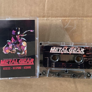 May include: A clear cassette tape case and cassette featuring the game Metal Gear Solid. The case has a black background with a character illustration and the game title in red. The cassette tape has the game title in white.