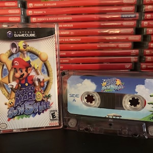 May include: A Nintendo GameCube game case for "Super Mario Sunshine" next to a cassette tape with the same title. The game case features Mario in a blue jumpsuit and red hat. The cassette tape has a tropical scene.
