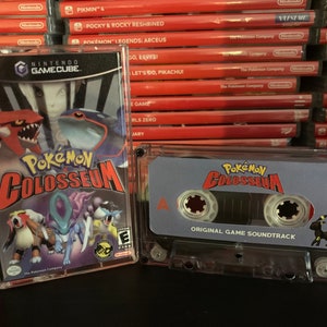 May include: A Nintendo GameCube game case and a cassette tape of the original soundtrack for Pokémon Colosseum. The game case features various Pokémon characters. The cassette tape has the game's logo and a black Umbreon illustration.