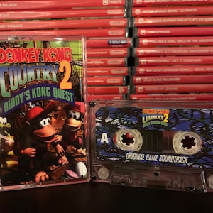 Puede incluir: Un estuche de plástico transparente que contiene el cartucho del videojuego Donkey Kong Country 2: Diddy's Kong Quest. La carátula del juego presenta a Donkey Kong y Diddy Kong. También se ve la cinta de casete de la banda sonora original.