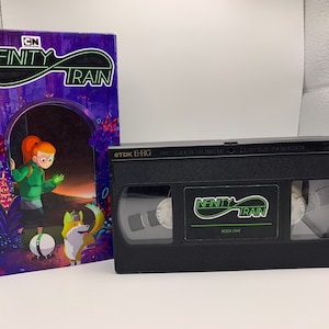 May include: A black VHS tape and a book with the title "Infinity Train". The tape has the show's logo and the words "Book One". The book cover features a girl with red hair and a dog.