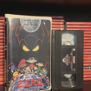 May include: A VHS tape and case for the animated film "Codename: Kids Next Door - Operation Z.E.R.O." The case features a dark background with the film's title and characters. The tape is black with white text.