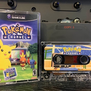 May include: A Nintendo GameCube game case and a cassette tape, both featuring "Pokémon Channel" branding. The game case shows Pikachu and other Pokémon characters. The cassette tape has a matching design with the game's logo and imagery.