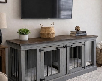 May include: A gray wooden dog crate with two compartments, each with a metal bar door and a soft bed. The crate has a dark wood top, and is topped with a plant, a basket, and books. A TV is mounted above.