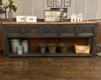 May include: A black console table with four drawers and a lower shelf. The table has a distressed wood finish and is decorated with metal buckets, a woven basket, and white boxes. The sign above the table reads "grateful".