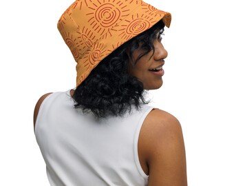 May include: A person wearing a light orange bucket hat with a red sun design. The hat has a wide brim and is made of a soft, comfortable fabric.