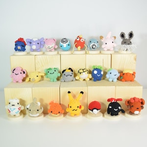 May include: A collection of colorful, handmade crochet figures displayed on wooden blocks. The figures include various creatures in shades of blue, pink, yellow, orange, and gray. Each figure is unique, with distinct features and details.