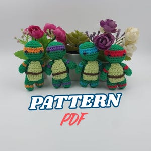May include: Four crocheted Teenage Mutant Ninja Turtle amigurumi figures with different colored masks. The figures are green with brown shells and are standing on a white surface. The text "PATTERN PDF" is written in red and blue letters below the figures.