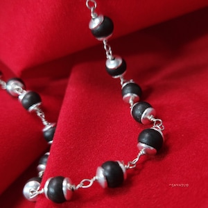 May include: A silver chain necklace with black wooden beads. The necklace is on a red velvet background.