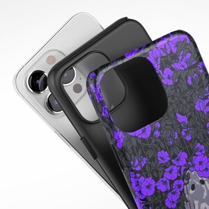 May include: Three phone cases, one clear, one black, and one with a purple floral pattern. The floral pattern case has a small animal peeking out from behind the flowers.