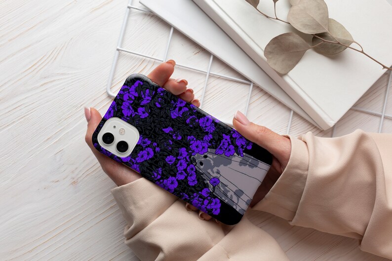 May include: A black phone case with a purple floral design and a white and gray abstract design. The case has a camera lens cutout.