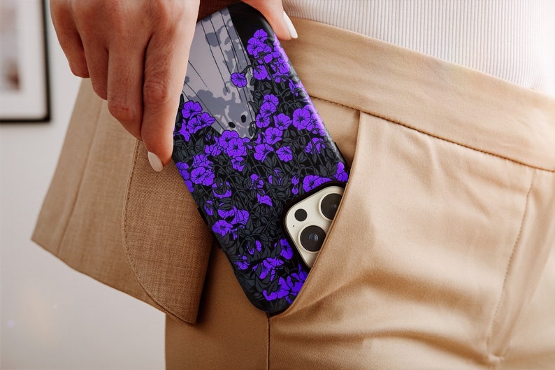 May include: A black phone case with a floral design featuring purple flowers on a black background. The case is in a person's pocket.