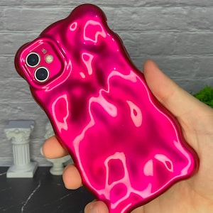 May include: A bright pink phone case with a liquid-like, abstract design. The case is made of a glossy material and has a smooth, flowing texture.