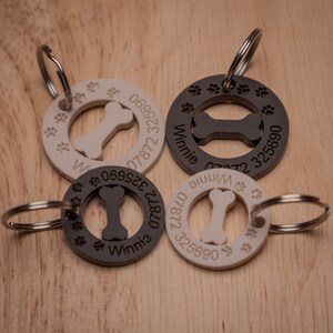 Puede incluir: Cuatro chapas para perros con una forma de hueso recortada en el centro. Dos chapas son negras con texto blanco y dos chapas son blancas con texto negro. Cada chapa tiene un anillo para sujetar al collar y el texto "Winnie" y un n&uacute;mero de tel&eacute;fono.