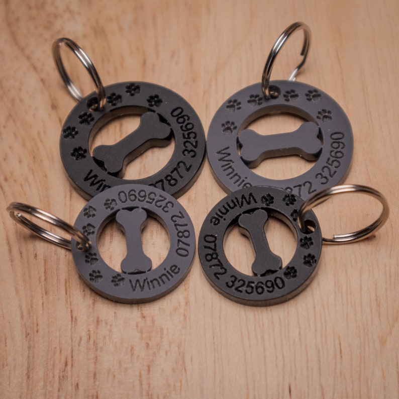 Puede incluir: Cuatro chapas para perros de metal negro con huellas de patas y un dise&ntilde;o de hueso. Las chapas est&aacute;n grabadas con el nombre "Winnie" y un n&uacute;mero de tel&eacute;fono.