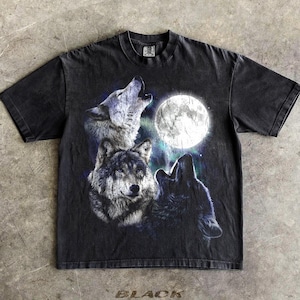 Pode incluir: Camiseta preta com um gráfico de três lobos uivando para a lua cheia. O design inclui tons de cinza, branco e azul. A palavra "BLACK" está impressa na parte inferior da camiseta.