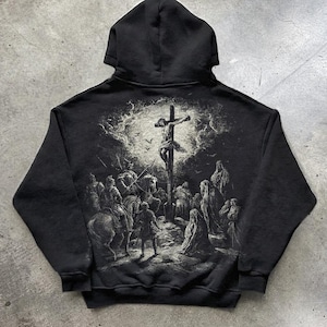Puede incluir: Sudadera con capucha negra con un gráfico detallado en blanco y negro en la espalda que representa una escena de crucifixión. El diseño presenta un uso dramático de la luz y la sombra. La palabra "BLACK" está impresa en la parte inferior.
