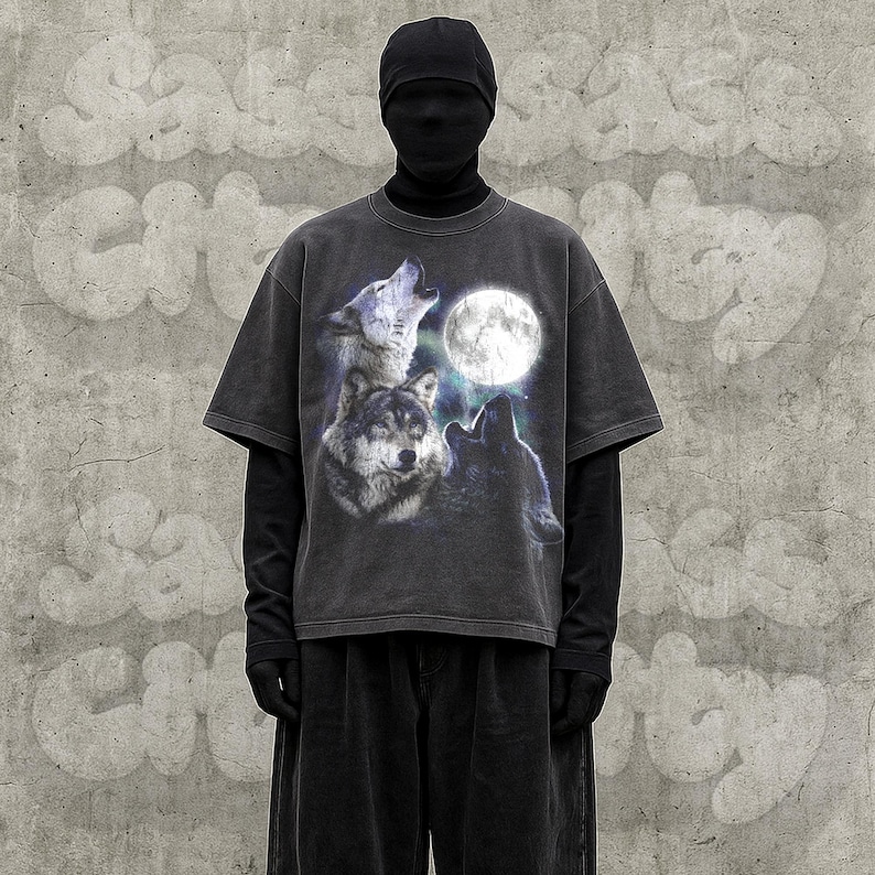 K&ouml;nnte beinhalten: Dunkelgraues T-Shirt mit einer Grafik von drei W&ouml;lfen, die einen Vollmond anheulen. Das Shirt hat einen Vintage-Look. Das Model tr&auml;gt einen schwarzen Rollkragenpullover und eine schwarze Hose.