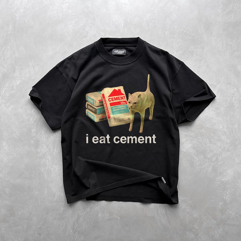 May include: Black t-shirt with a graphic of a cat looking at a stack of cement bags. The text "i eat cement" is printed below the image.