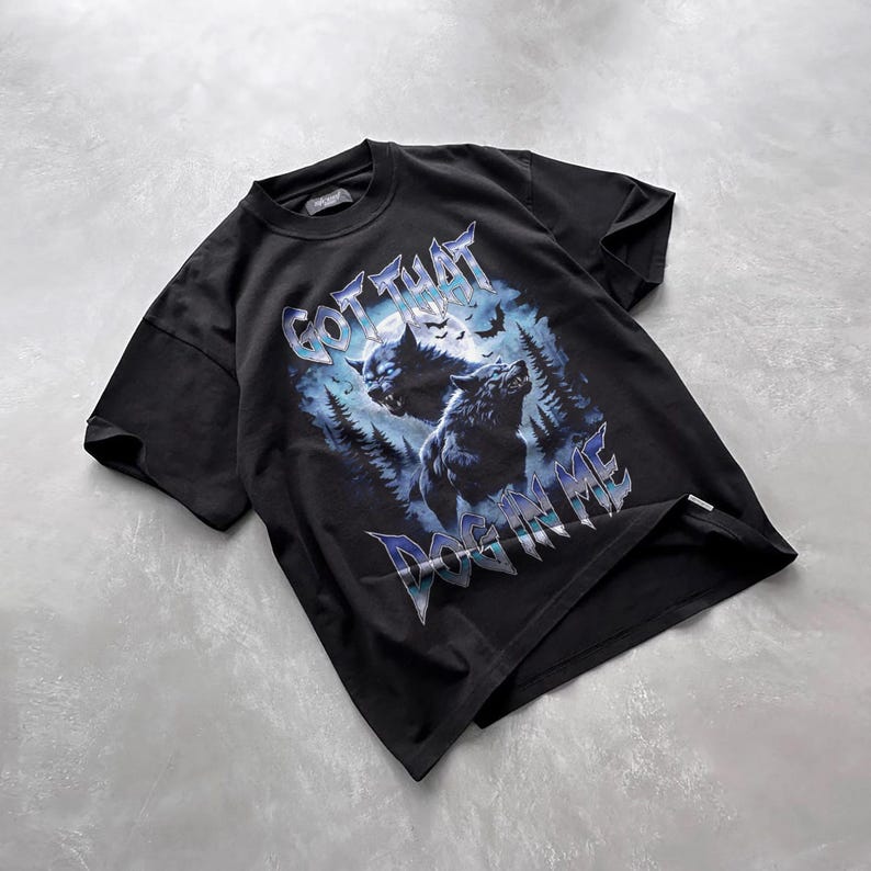 Pode incluir: Camiseta preta com uma estampa gr&aacute;fica de dois lobos uivando para a lua em uma floresta. O texto "GOT THAT DOG IN ME" &eacute; impresso em uma fonte met&aacute;lica abaixo dos lobos.