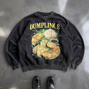 Könnte beinhalten: Ein schwarzes Sweatshirt mit Rundhalsausschnitt und einem Grafikdruck von verschiedenen Teigtaschen sowie einer kleinen Schale mit Dip. Das Wort DUMPLINGS ist in gelben Großbuchstaben darüber gedruckt, umgeben von grünen Blitzen.