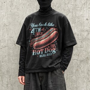 May include: Black graphic t-shirt with the text "You look like the 4th of July makes me want a hot dog real bad" and a hot dog illustration. The shirt has short sleeves and a vintage style.