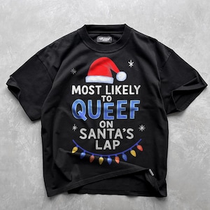 May include: Black t-shirt with the text "MOST LIKELY TO QUEEF ON SANTA'S LAP" in white and blue, featuring a Santa hat and string of lights. A humorous Christmas-themed graphic tee.