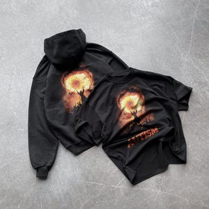 Puede incluir: Dos sudaderas con capucha negras con un estampado gr&aacute;fico de una persona sosteniendo un orbe en llamas. El gr&aacute;fico en la sudadera con capucha de la izquierda tiene el texto "AUTISM" impreso debajo.