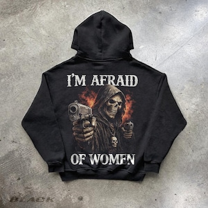 May include: A black hooded sweatshirt featuring a graphic print of a hooded skeleton figure holding two handguns. The text "I'M AFRAID OF WOMEN" is printed in white above and below the central illustration, which includes orange smoke effects.