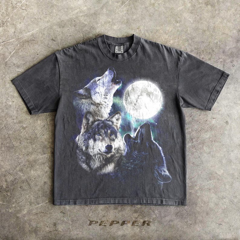 K&ouml;nnte beinhalten: Dunkelgraues T-Shirt mit einer Grafik von drei W&ouml;lfen, die den Vollmond anheulen. Das Design beinhaltet Blau-, Wei&szlig;- und Schwarzt&ouml;ne. Das Wort "PEPPER" ist am unteren Rand des Shirts aufgedruckt.