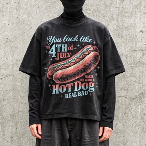 May include: Black graphic t-shirt with the text "You look like the 4th of July makes me want a hot dog real bad" and a hot dog illustration. The shirt has short sleeves and a vintage style.