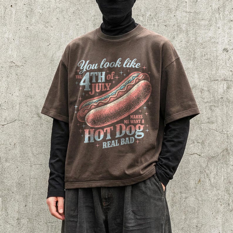 May include: Brown t-shirt with a distressed graphic featuring a hot dog and the text "You look like the 4th of July makes me want a hot dog real bad." The shirt has short sleeves.