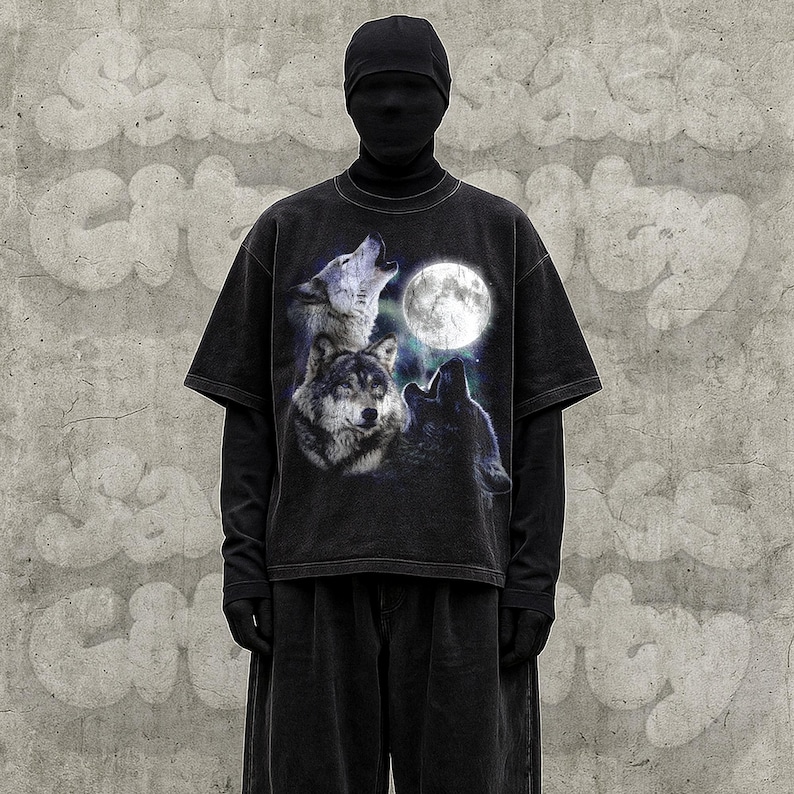 K&ouml;nnte beinhalten: Schwarzes T-Shirt mit einer Grafik von drei W&ouml;lfen, die einen Vollmond anheulen. Das Shirt wird &uuml;ber einem schwarzen Langarmshirt und einer schwarzen Hose getragen. Der Hintergrund ist eine graue Betonmauer.