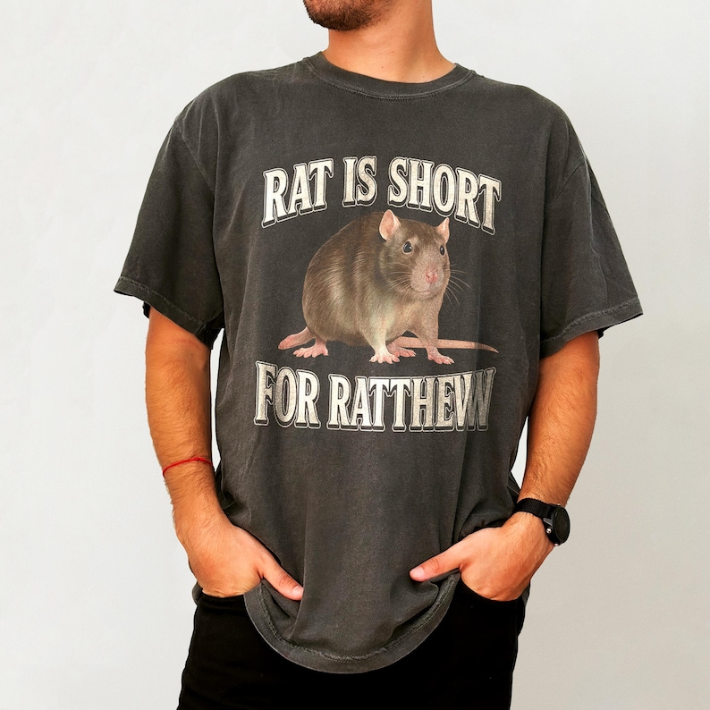 May include: A dark gray t-shirt with a rat graphic and the text "Rat is short for Ratthew".