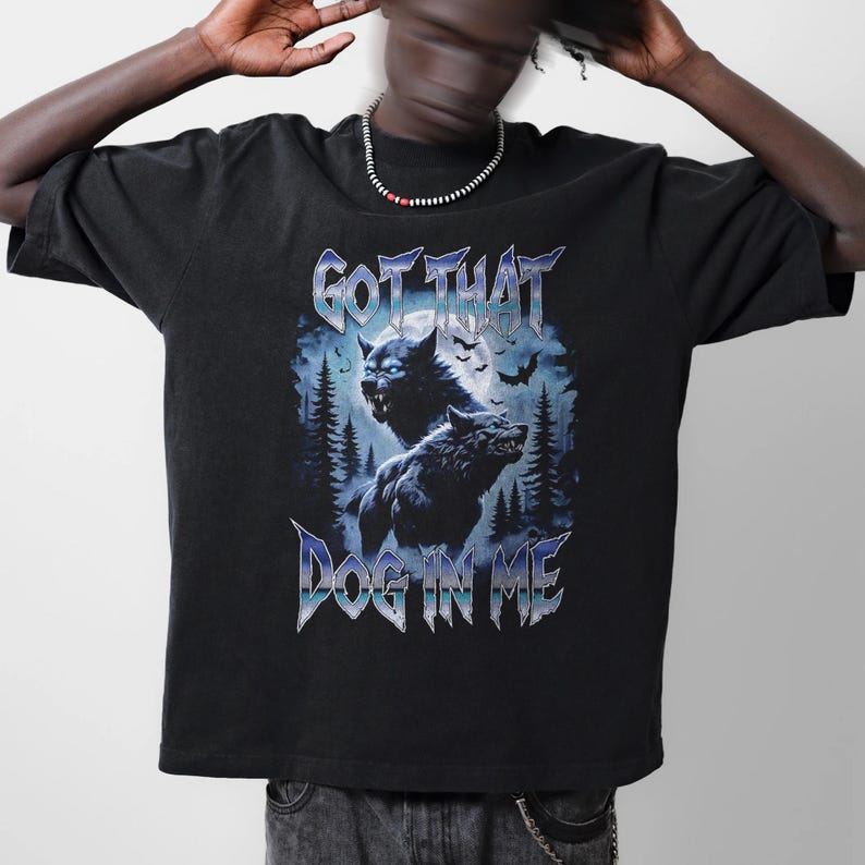 Pode incluir: Camiseta preta com um gr&aacute;fico de dois lobos uivando para a lua. O texto "Got That Dog In Me" &eacute; impresso abaixo dos lobos.