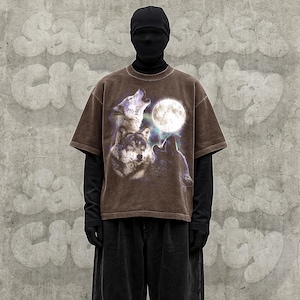 K&ouml;nnte beinhalten: Braunes T-Shirt mit einem Wolfsrudel, das den Vollmond anheult. Das Grafik-T-Shirt hat einen Vintage-Look. Das Shirt wird &uuml;ber einem schwarzen Langarmshirt und einer schwarzen Hose getragen.