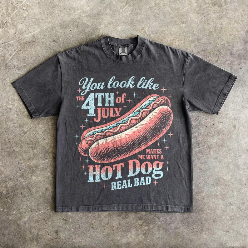 May include: Dark gray t-shirt with a graphic of a hot dog and the text "You look like the 4th of July makes me want a hot dog real bad." The design features red, blue, and white colors.