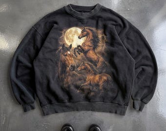 May include: A black crewneck sweatshirt featuring a graphic print of three brown horses in a field under a large full moon and lightning. The sweatshirt has long sleeves, a ribbed collar, and ribbed cuffs, showcasing a dark, weathered aesthetic.