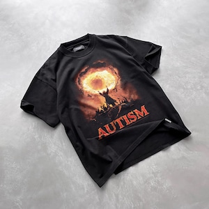 Puede incluir: Camiseta negra con un estampado gr&aacute;fico de una persona sosteniendo un anillo en llamas con la palabra "AUTISMO" impresa debajo.