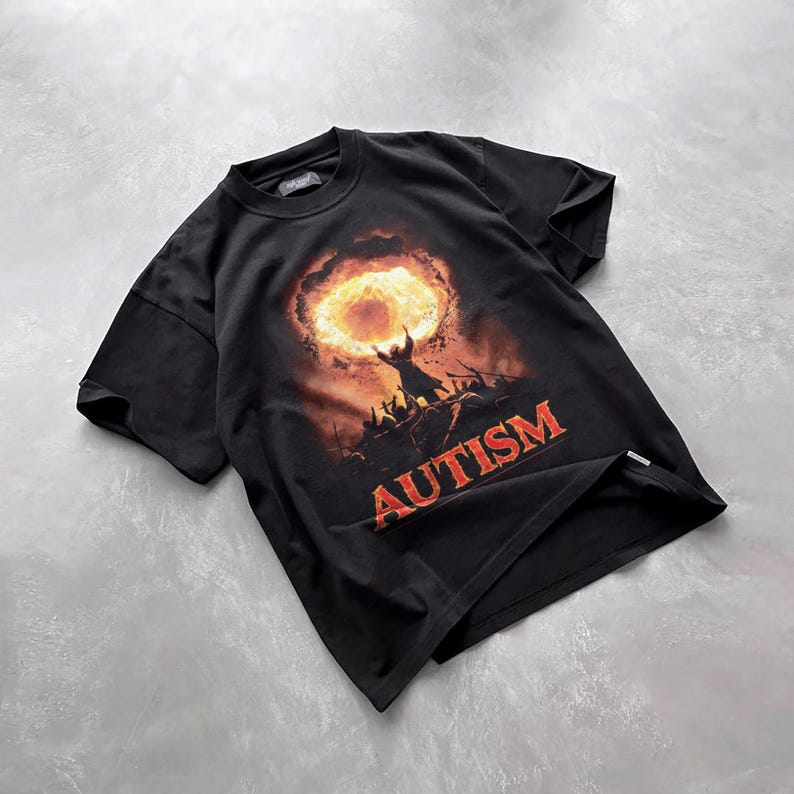 Puede incluir: Camiseta negra con un estampado gr&aacute;fico de una persona sosteniendo un anillo en llamas con la palabra "AUTISMO" impresa debajo.
