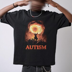 Puede incluir: Camiseta negra con un gr&aacute;fico de una persona sosteniendo un c&iacute;rculo en llamas y la palabra "AUTISM" impresa debajo.